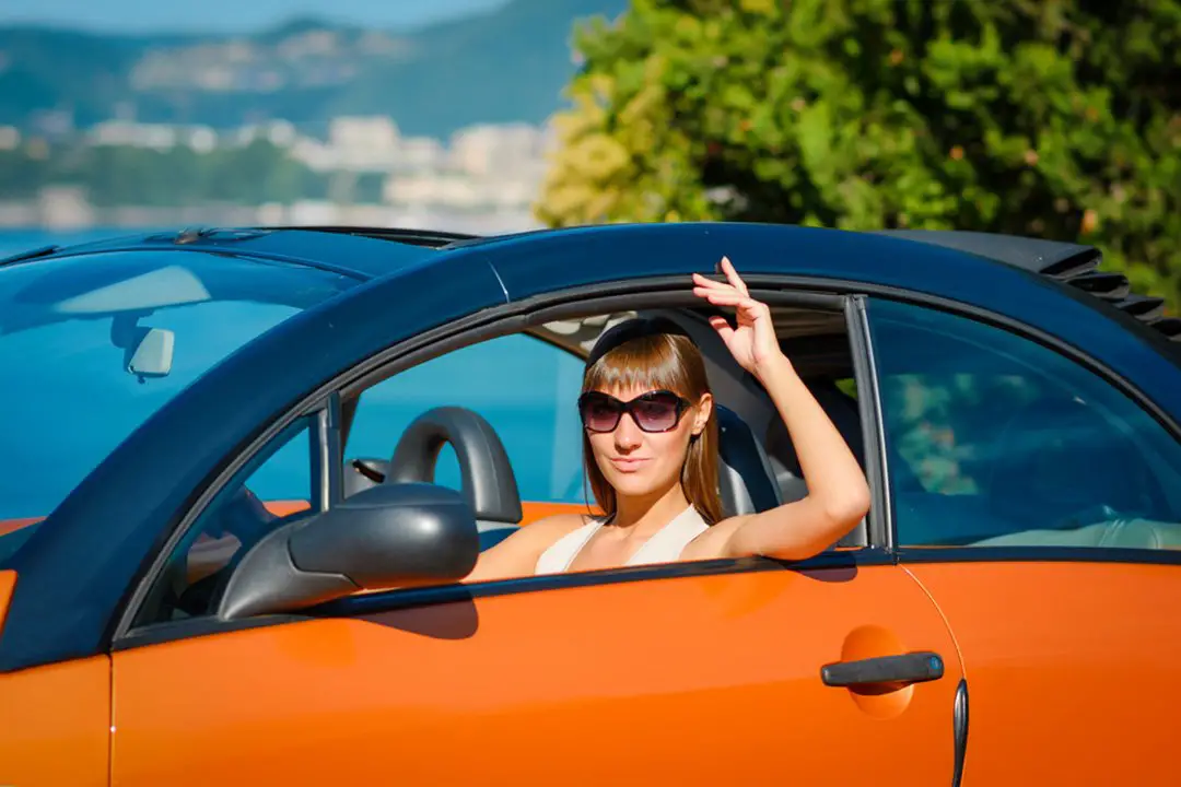 Beautiful-young-woman-with-long-hair-sitting-and-smiling-in-orange-cabriolet-at-the-Mediterranean-sea-coast