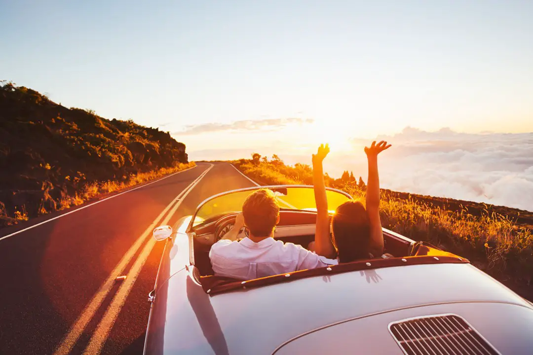 Happy-Couple-Driving-on-Country-Road-into-the-Sunset-in-Classic-Vintage-Sports-Car